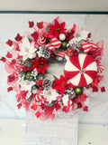 Red and white candy cane Christmas wreath with an oversized peppermint decoration, striped bows, flowers, baubles and frosted pine cones