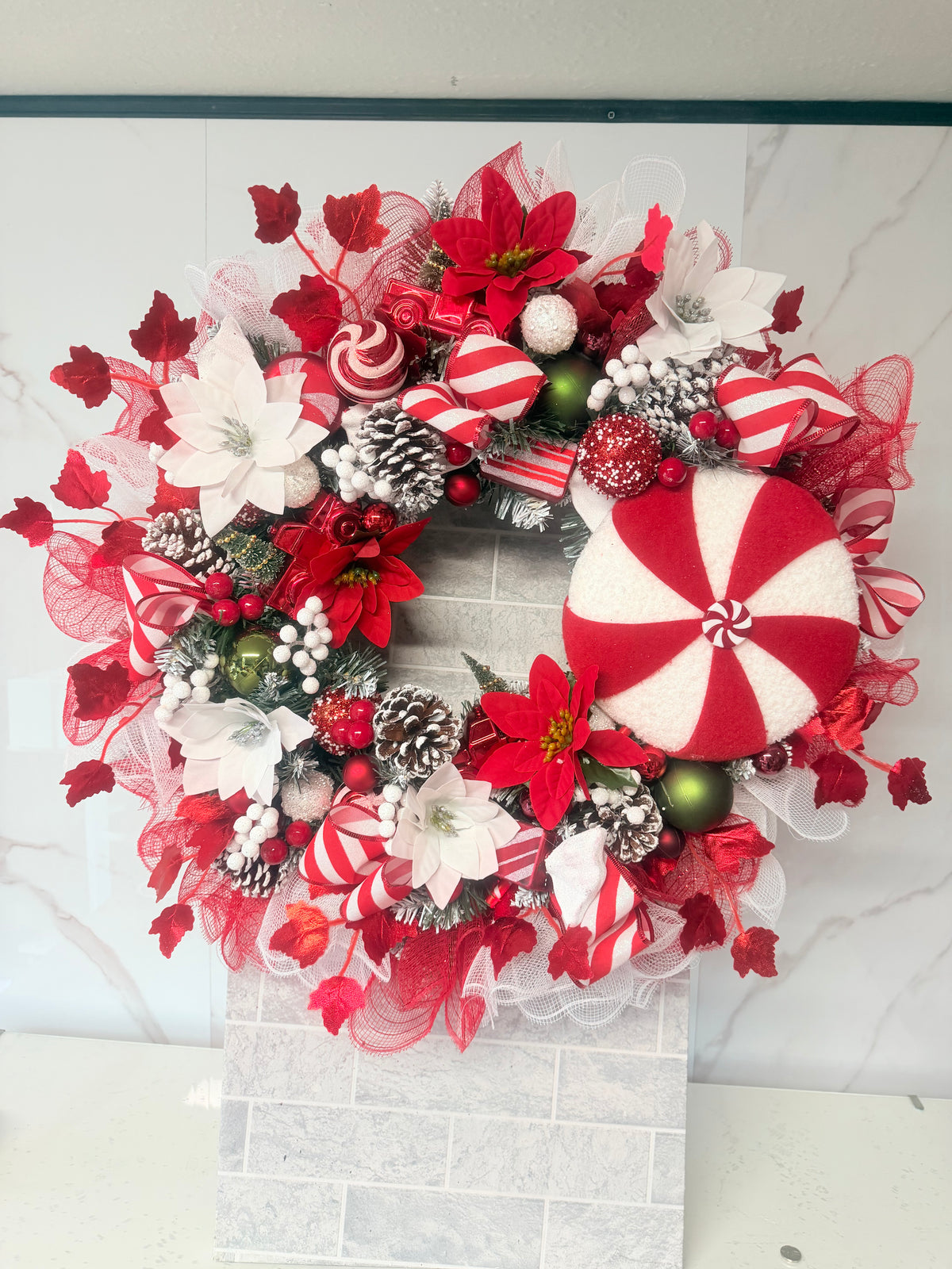 Red and white candy cane Christmas wreath with an oversized peppermint decoration, striped bows, flowers, baubles and frosted pine cones