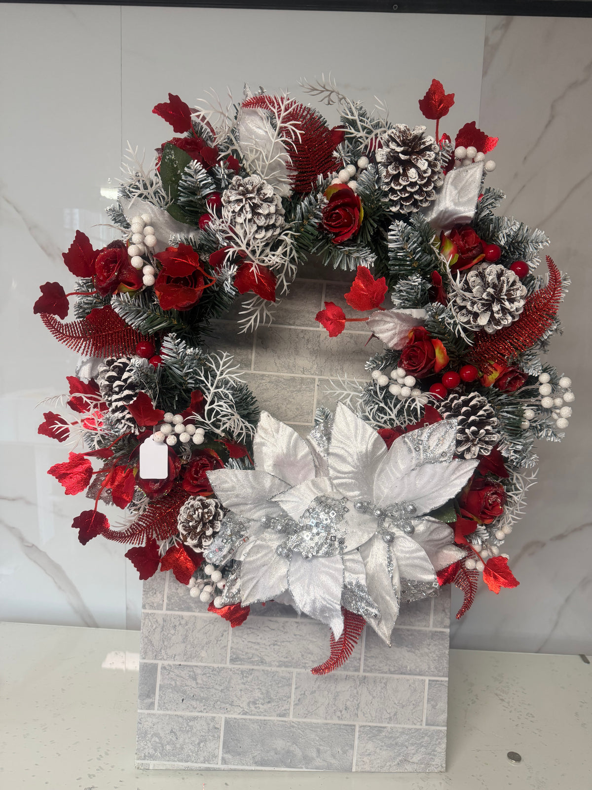 Red and white frosted Christmas wreath with red roses, white poinsettia-style flowers, decorative berries and snow-dusted pine cones
