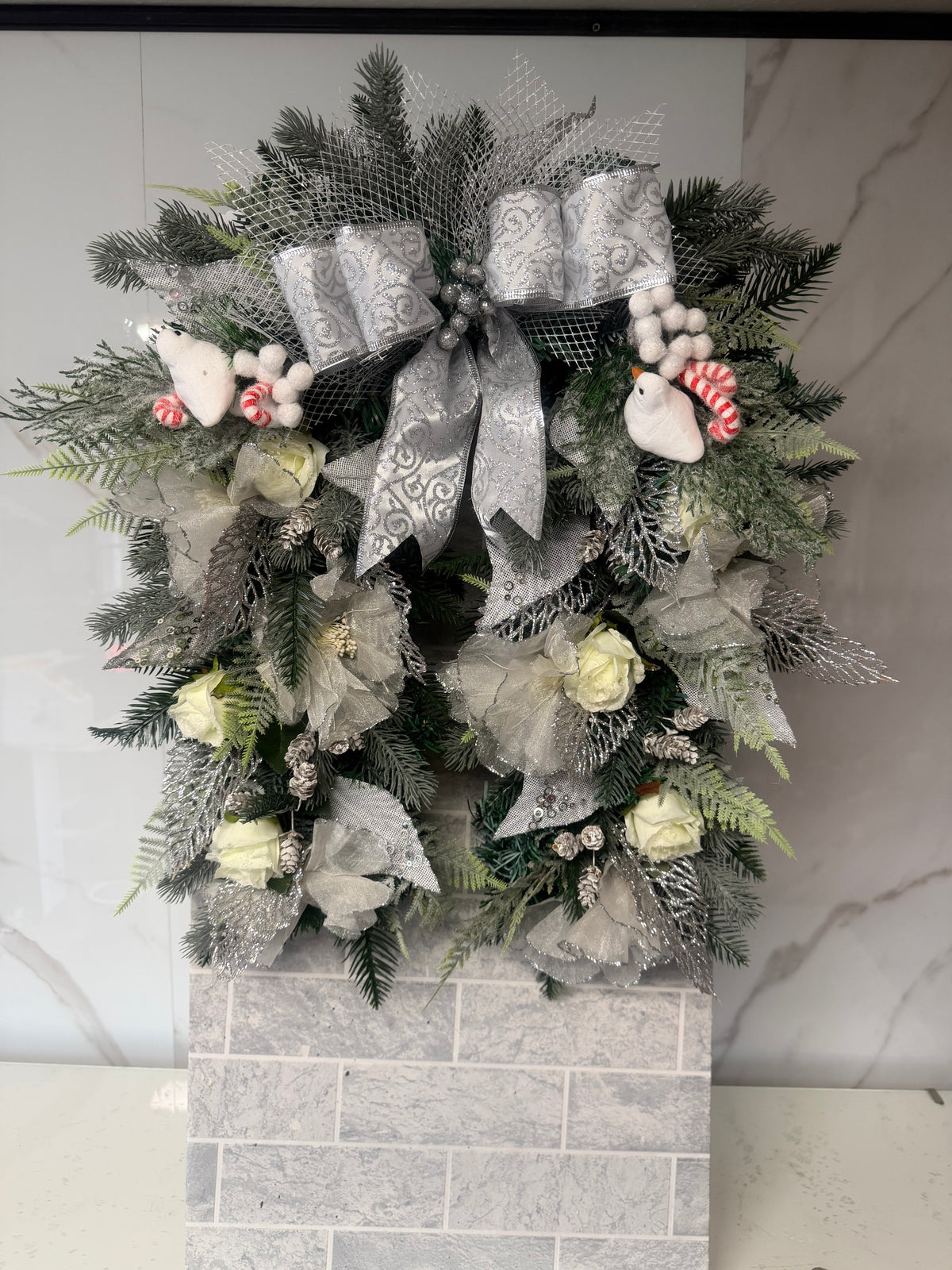 Silver and ivory horseshoe Christmas wreath with ivory flowers, frosted greenery, a silver bow and white bird decorations