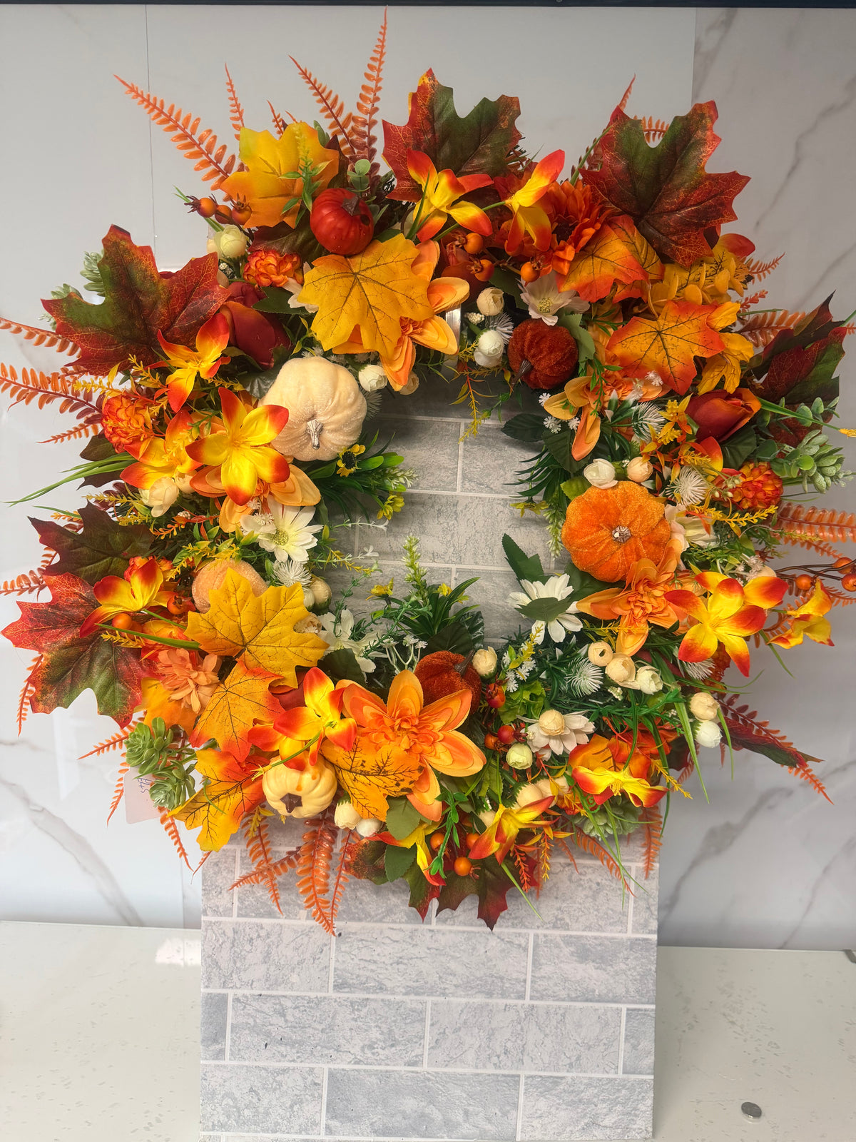 Full autumn wreath with orange and cream pumpkins, orange and yellow flowers, autumn leaves and greenery