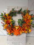 Autumn wreath with orange flowers, golden leaves, pumpkins and berries on a rustic twig-style base