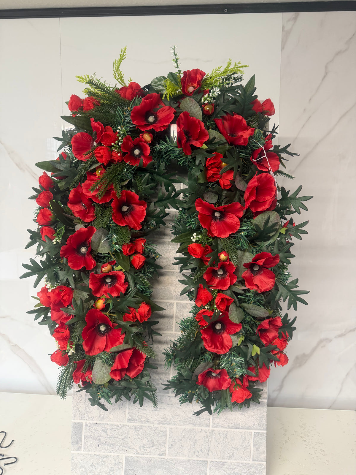 Horseshoe-shaped wreath of red poppies and mixed green foliage