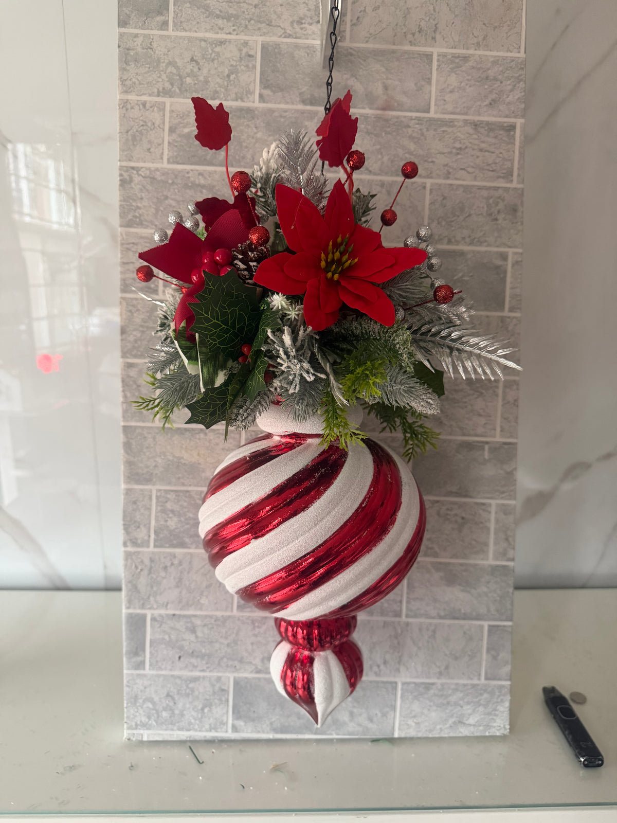 Red and white striped Christmas hanging ornament with artificial red flowers, berries and silver-toned foliage