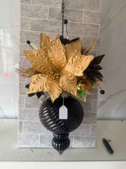 Black and gold Christmas hanging arrangement with a large gold flower, black foliage and glossy black spiral-ridged ornament
