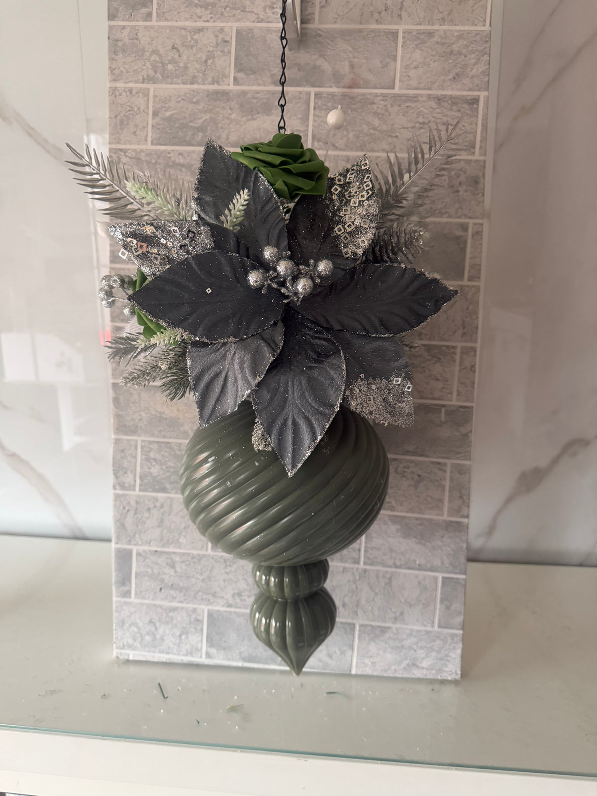 Charcoal and green Christmas hanging arrangement with a charcoal flower, green rose, silver foliage and dark green spiral ornament