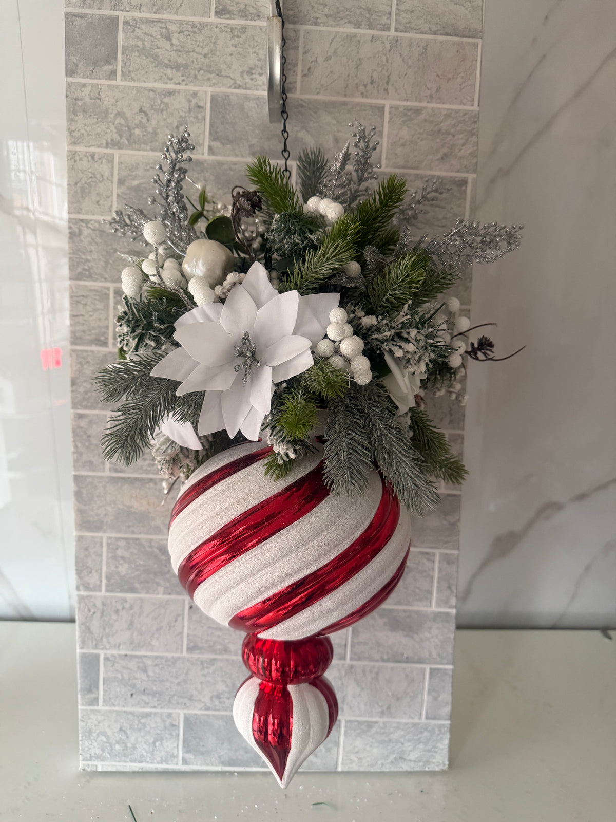 White poinsettia-style Christmas hanging arrangement with frosted greenery, white berries and a red-and-white striped ornament