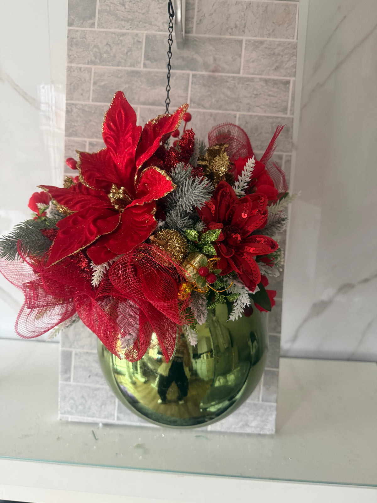 Red and green Christmas hanging arrangement with red flowers, frosted greenery, red mesh ribbon and a glossy green round bauble