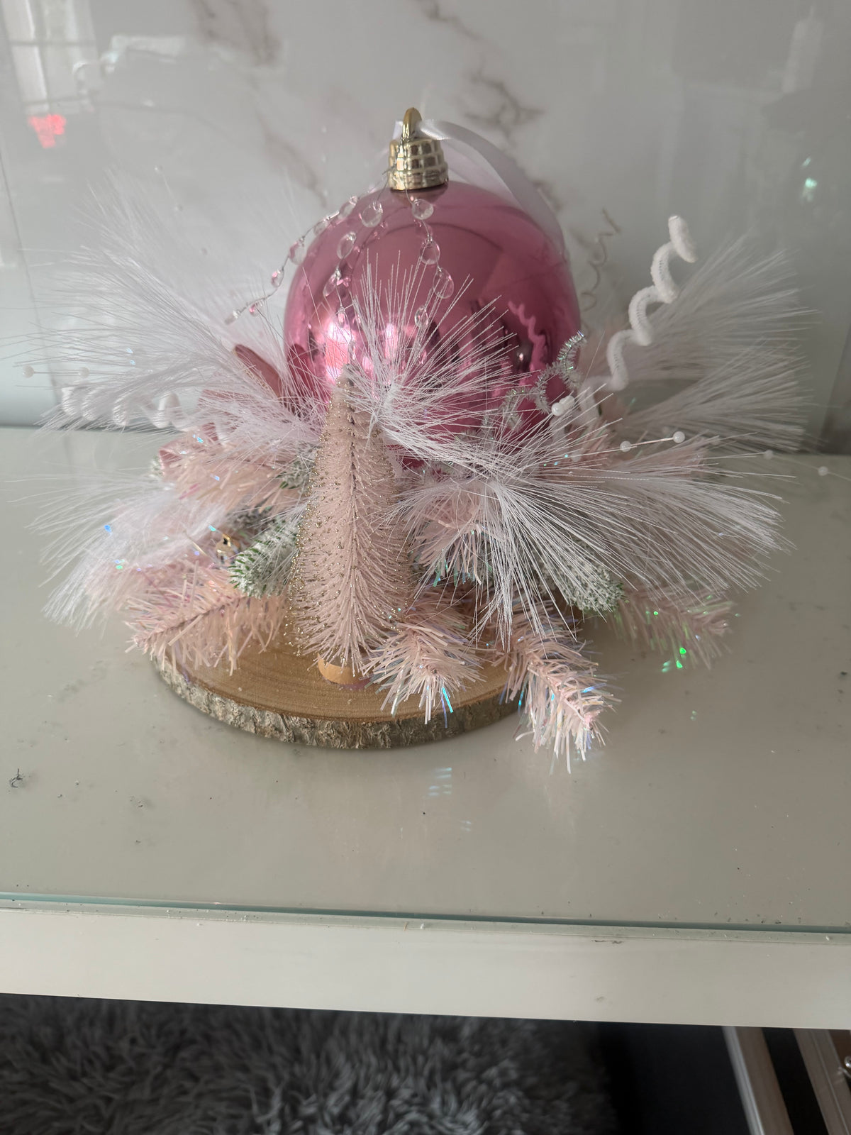 Pink bauble Christmas centrepiece with pale pink foliage and shimmering white sprays on a bark-edged wood slice