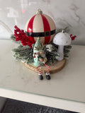 Christmas wood slice centrepiece with Santa-style striped bauble, green-hatted gnome, white mushroom and frosted foliage