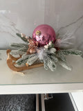 Wooden Christmas sleigh centrepiece with a glossy pink bauble, snowy greenery, white berries and rose-gold accents