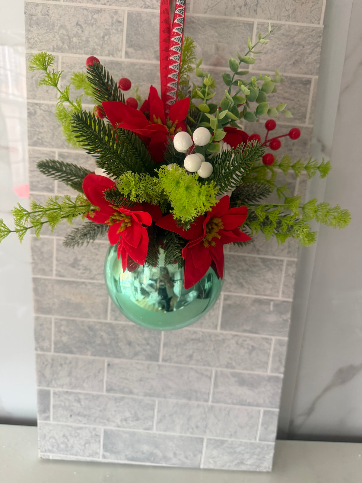 Christmas hanging arrangement with red poinsettias, greenery and a shiny green bauble
