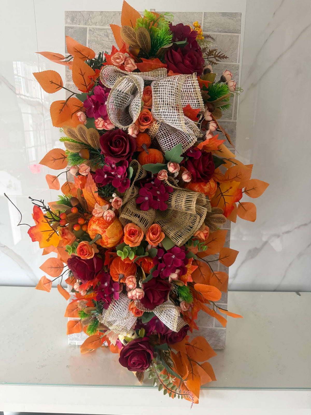 Autumn garland with burgundy and orange flowers, orange leaves, pumpkins and rustic mesh ribbon