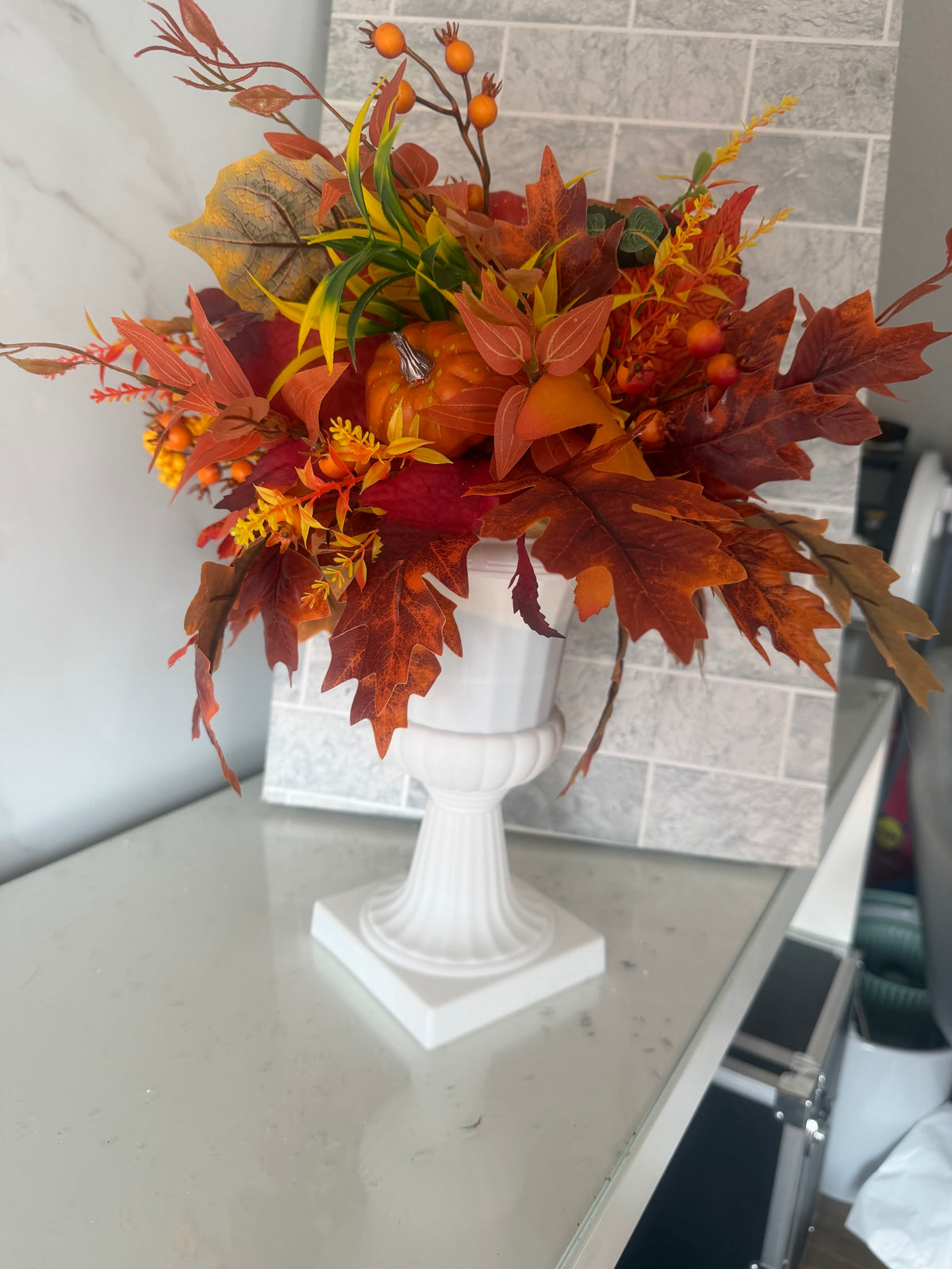 Autumn pumpkin and foliage arrangement with rust-coloured leaves and orange berries in a white pedestal vase
