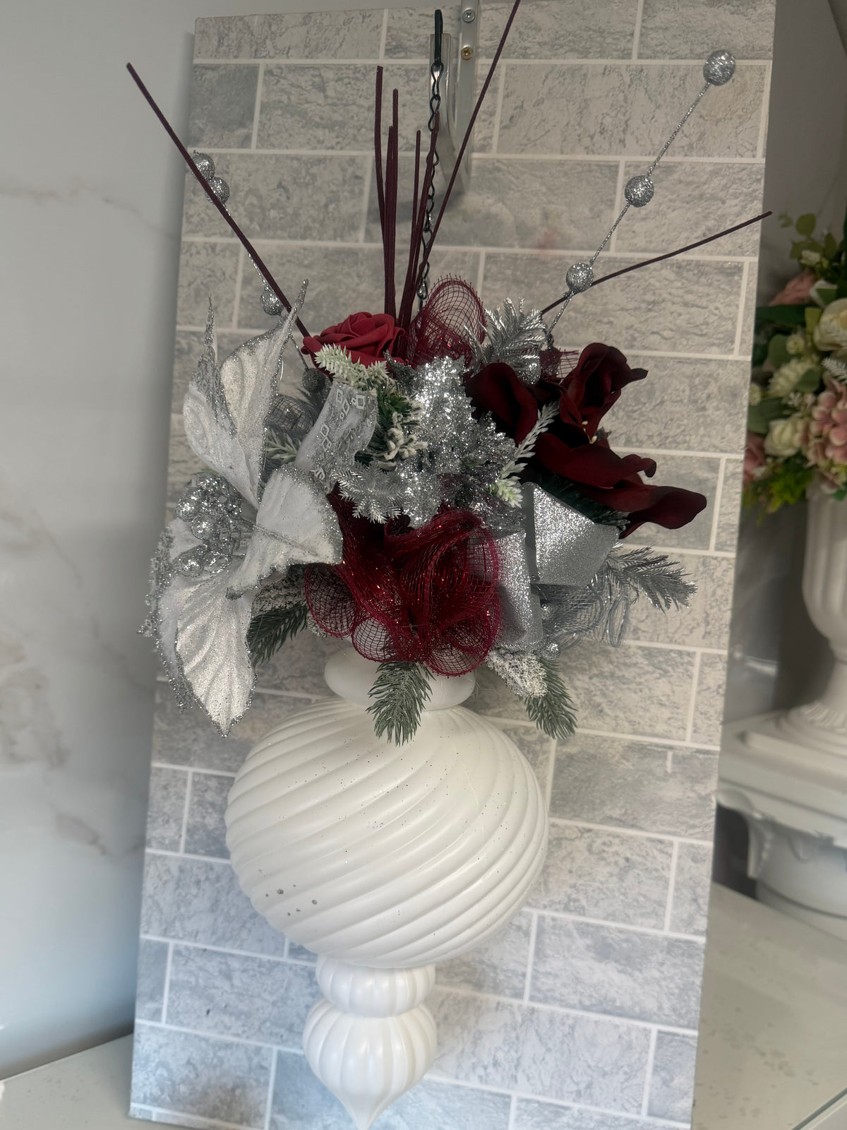 White ribbed Christmas hanging bauble with burgundy blooms, a silver-edged white flower, silver decorations and frosted greenery