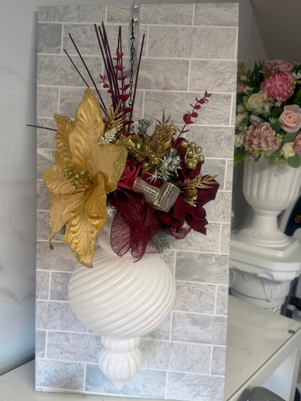 White ribbed hanging Christmas bauble with gold poinsettia-style flowers, burgundy blooms and festive greenery