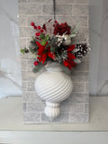 White ribbed Christmas bauble topped with red flowers, red berries, frosted greenery and a snow-dusted pine cone