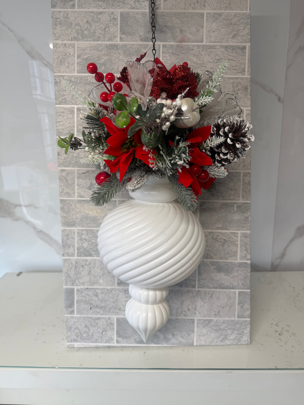 White ribbed Christmas bauble topped with red flowers, red berries, frosted greenery and a snow-dusted pine cone